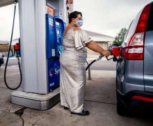 Professor Sami Schalk wearing a floor length silver dress, a silver sequin face mask, filling up a vehicle’s gas tank at a gas station.
