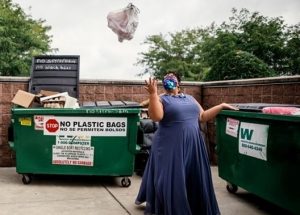 Professor Sami Schalk wearing a floor length purple dress, eyeglasses, and an iridescent sequin face mask tossing a bag of garbage over her shoulder