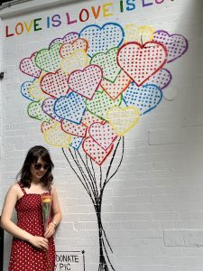 GWS student, Bianca Yue, holding flowers next to a Love is Love mural.