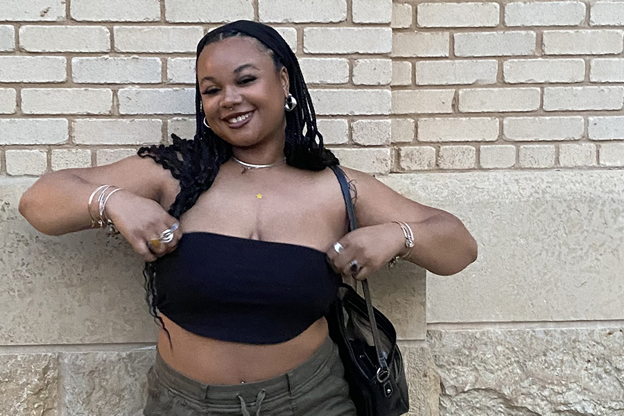Abigail Perkins smiles against a light brick backdrop wearing a black headband and wears a black top and khaki shorts.