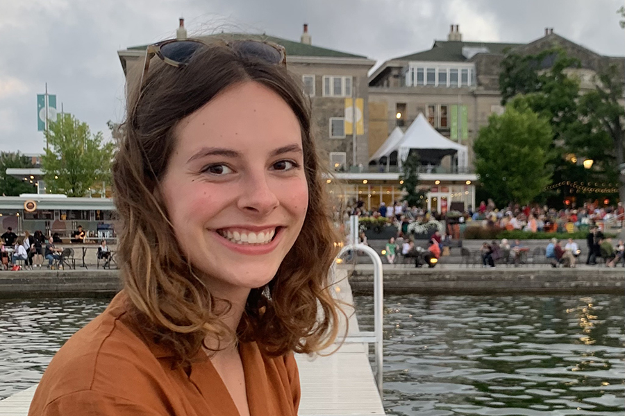 image of Amelia Weidemann sitting on a pier at the union with shoulder-length brown hair, smiling at the camera