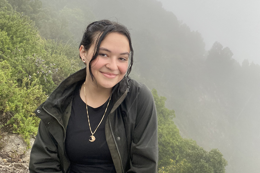 image of Ashlinn Thomas sitting outside with brown hair pulled back wearing a black top and black coat smiling at the camera