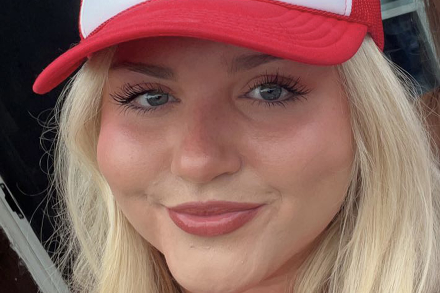 Caitlin Dolan smiles at the camera wearing a red-brimmed baseball cap in this close up.