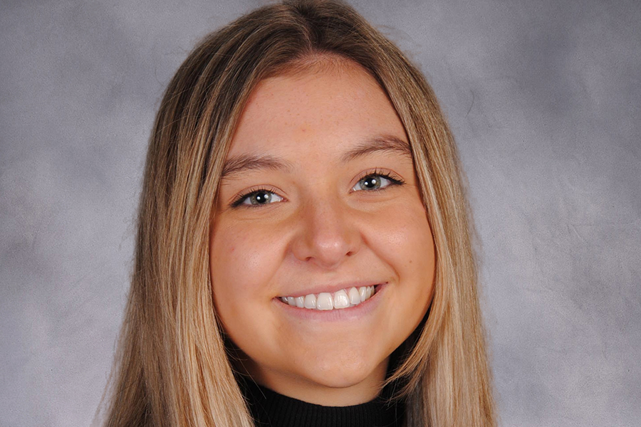 Drew Harris smiles in this portrait photo with a marbled grey background. Drew has long, dark blond hair.