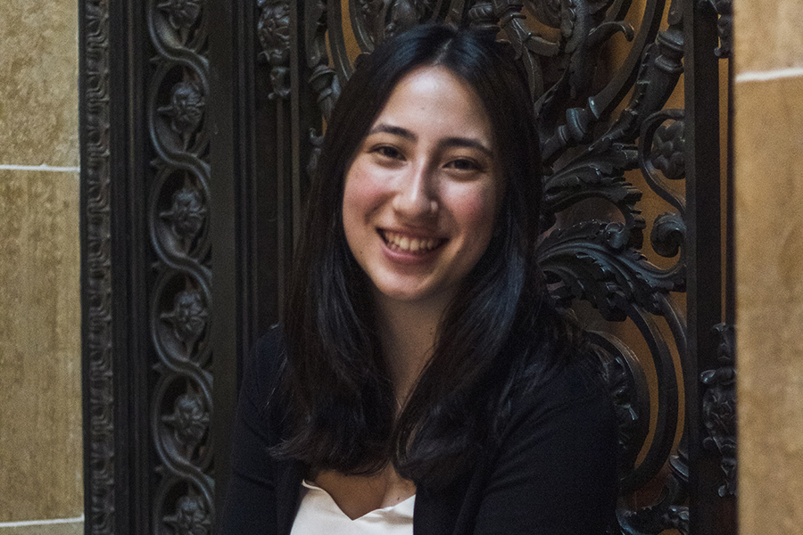 Emily Kurtin smiles in front of a wrought-iron background. Emily wears a white shirt and a black jacket.