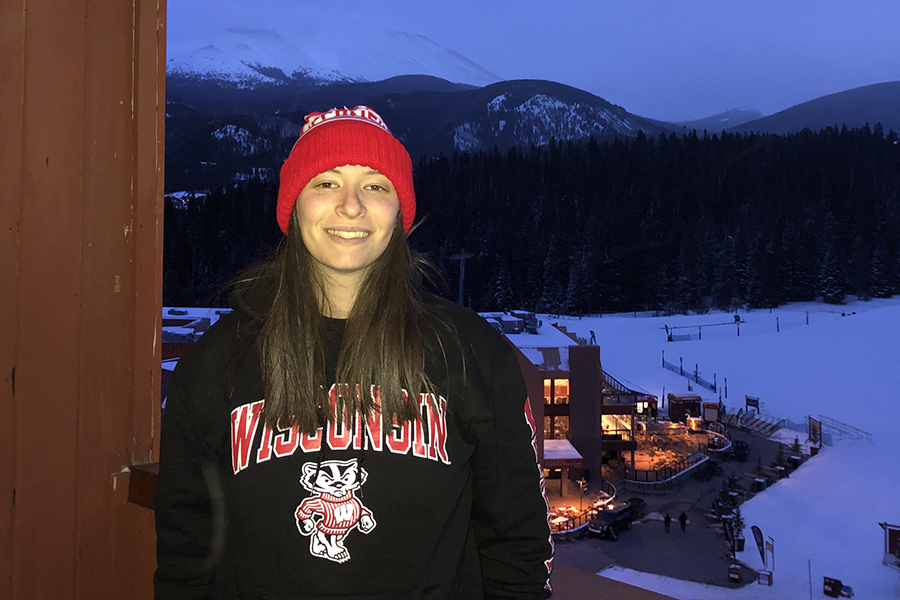 image of Jessie Taft with long brown hair wearing a red hat and a black Wisconsin Badger's sweatshirt smiling at the camera with mountains in the background at night