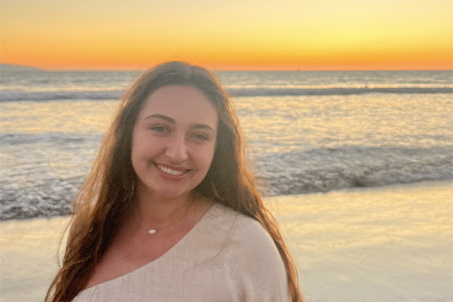 image of Kimberly Strathas with long brown hair and a white top smiling at the camera and standing in front of a body of water.