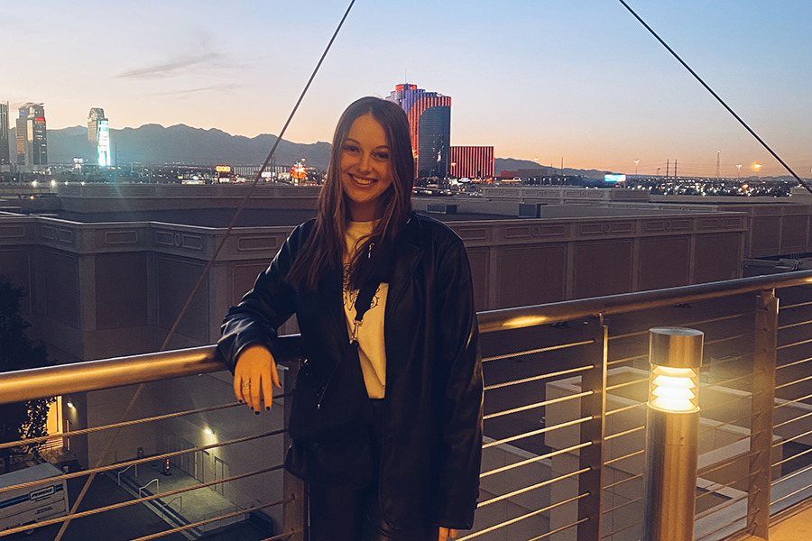Madison Schwartz stands against a railing, smiling, and with an urban backdrop.