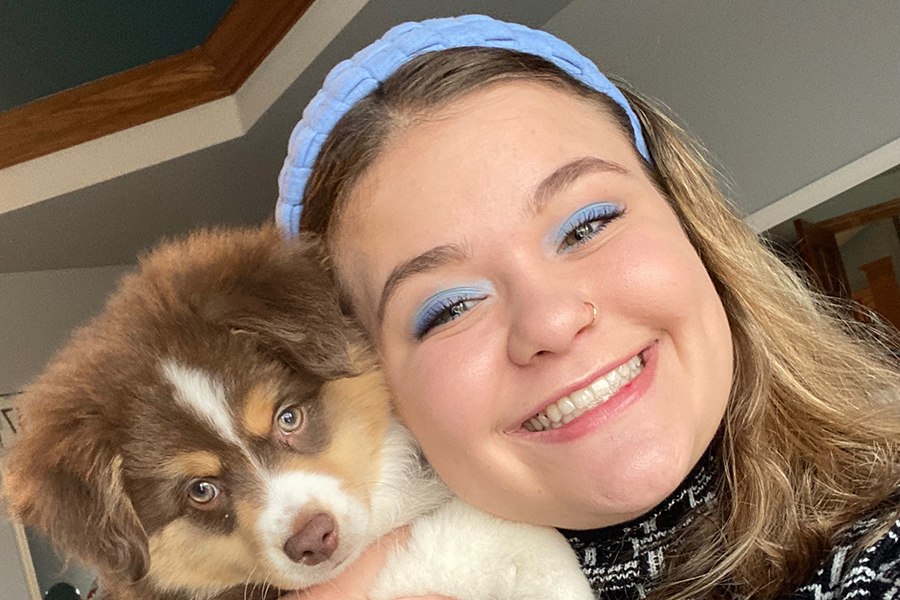 Stacy Ducheny grins at the camera wearing a pale blue headband holding a brown and white dog.