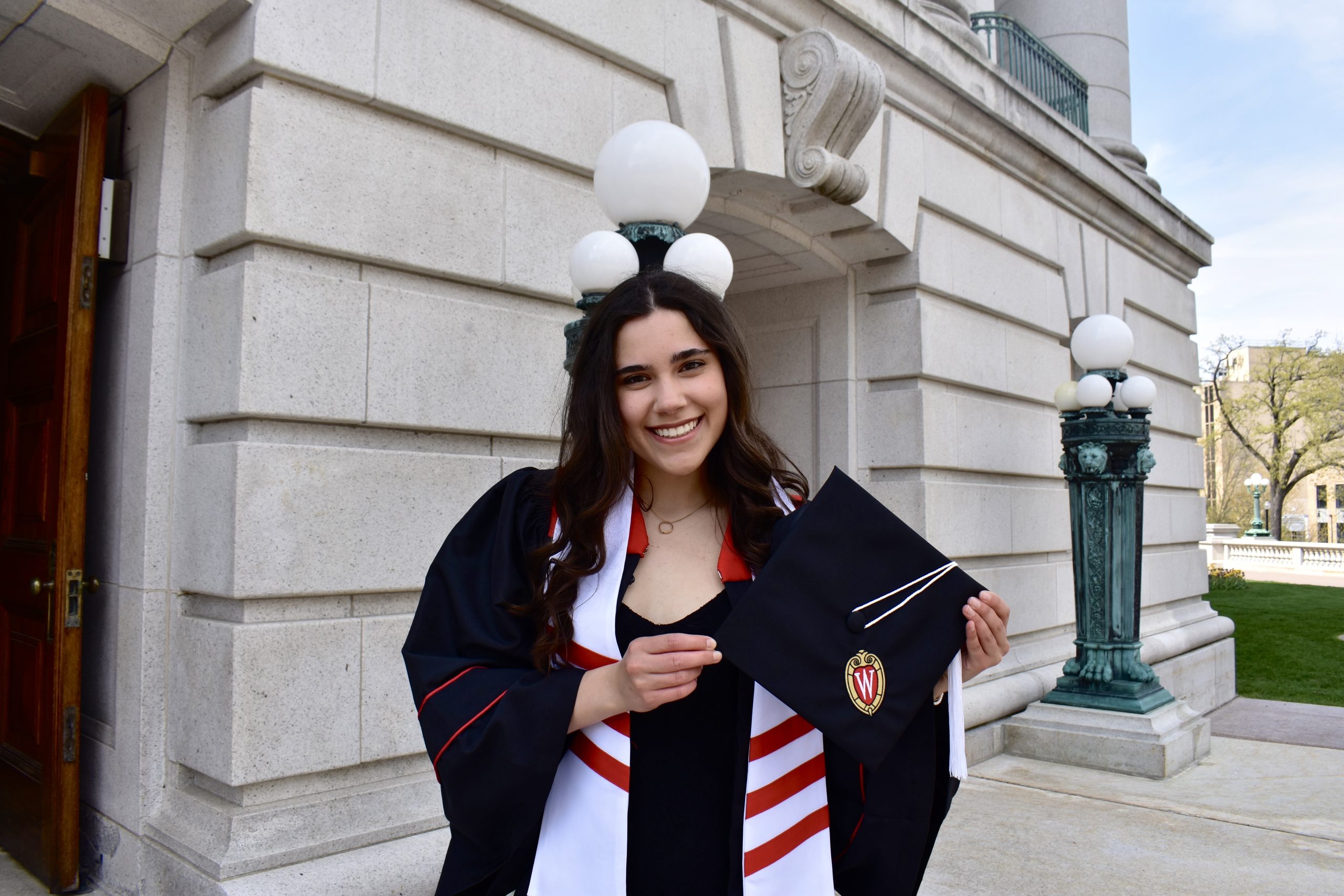 image of Isabella Ricker with long brown hair smiling at the camera wearing a graduation cap and gown.
