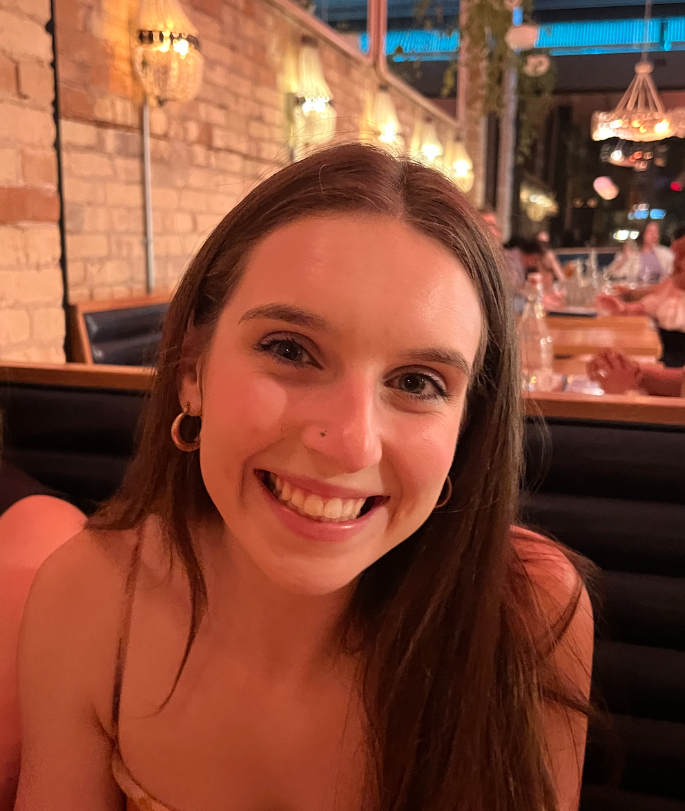 image of Lily Englebert sitting in a booth at a restaurant smiling at the camera with long brown hair