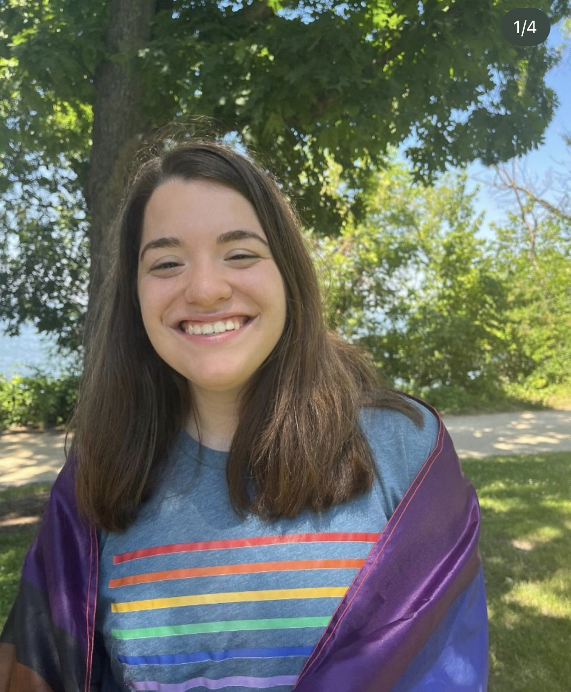 image of Natalia Iding with shoulder-length brown hair standing outside and smiling wearing a rainbow striped shirt