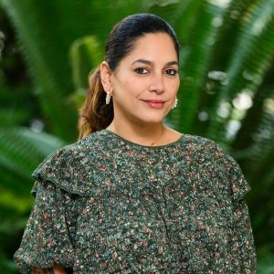 Image of professor Aurora Santiago Ortiz against greenery. She has a soft smile and wears a flower patterned shirt.